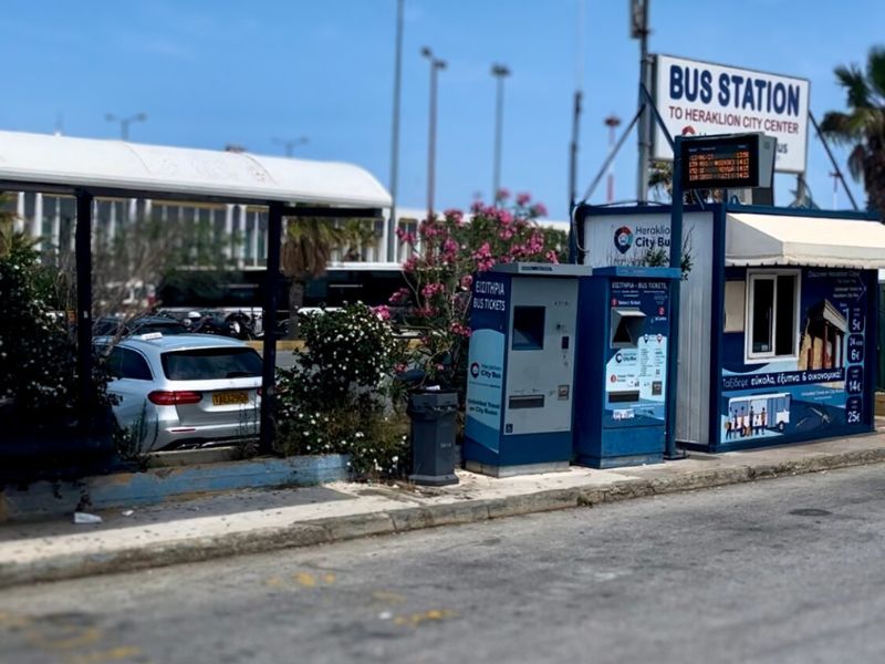 Fotografie autobusové zastávky do centra města Heraklion, která se nachází vlevo od příletové haly letiště Nikose Kazantzakise. Odsud jezdí městské autobusy MHD do centra Heraklionu, kde lze přestoupit na dálkové spoje směřující do Rethymna, Chanie nebo dalších částí Kréty.