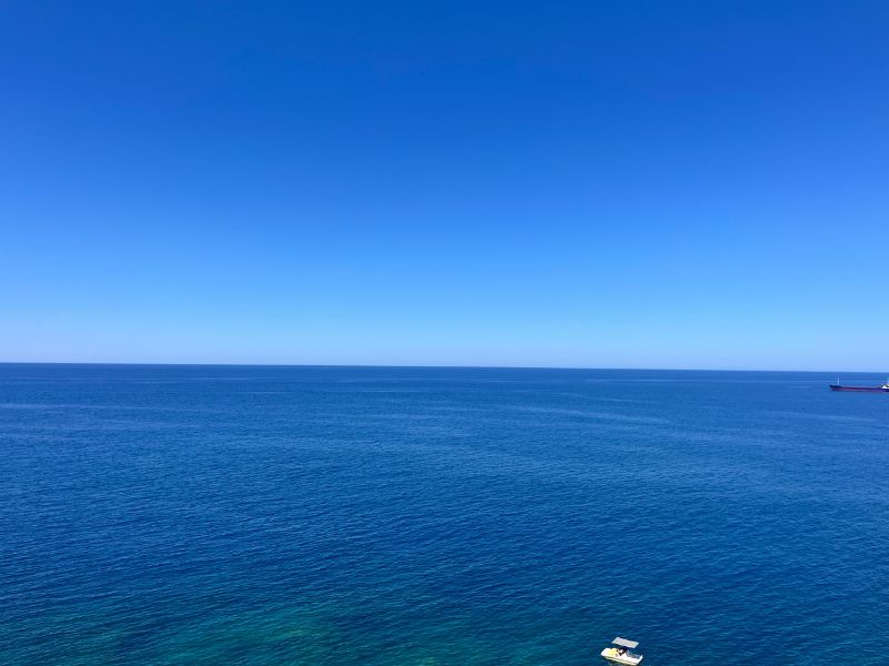 Pohled na nekonečné tyrkysové moře v letovisku Bali na Krétě s klidnou hladinou a panoramatickým horizontem.