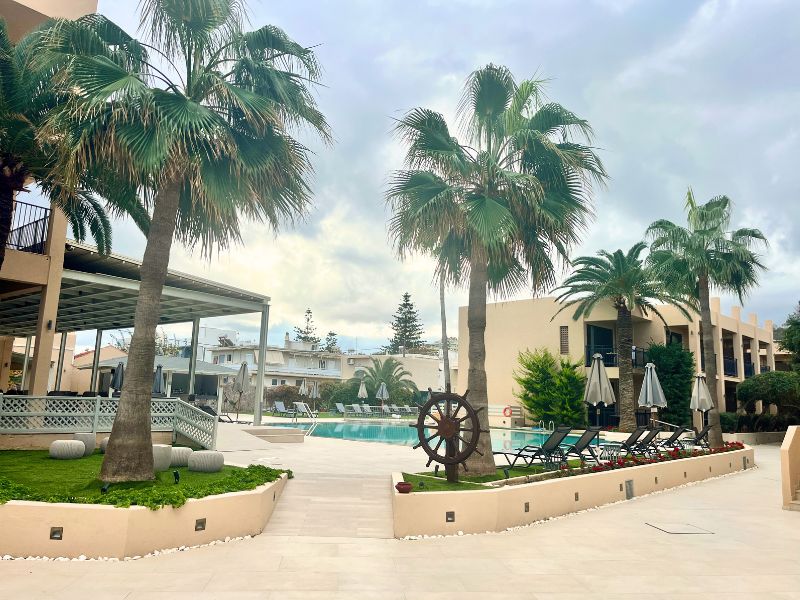 Hotelový bazén v Atlantis Beach Hotelu v Rethymnu na Krétě obklopený lehátky a palmami.